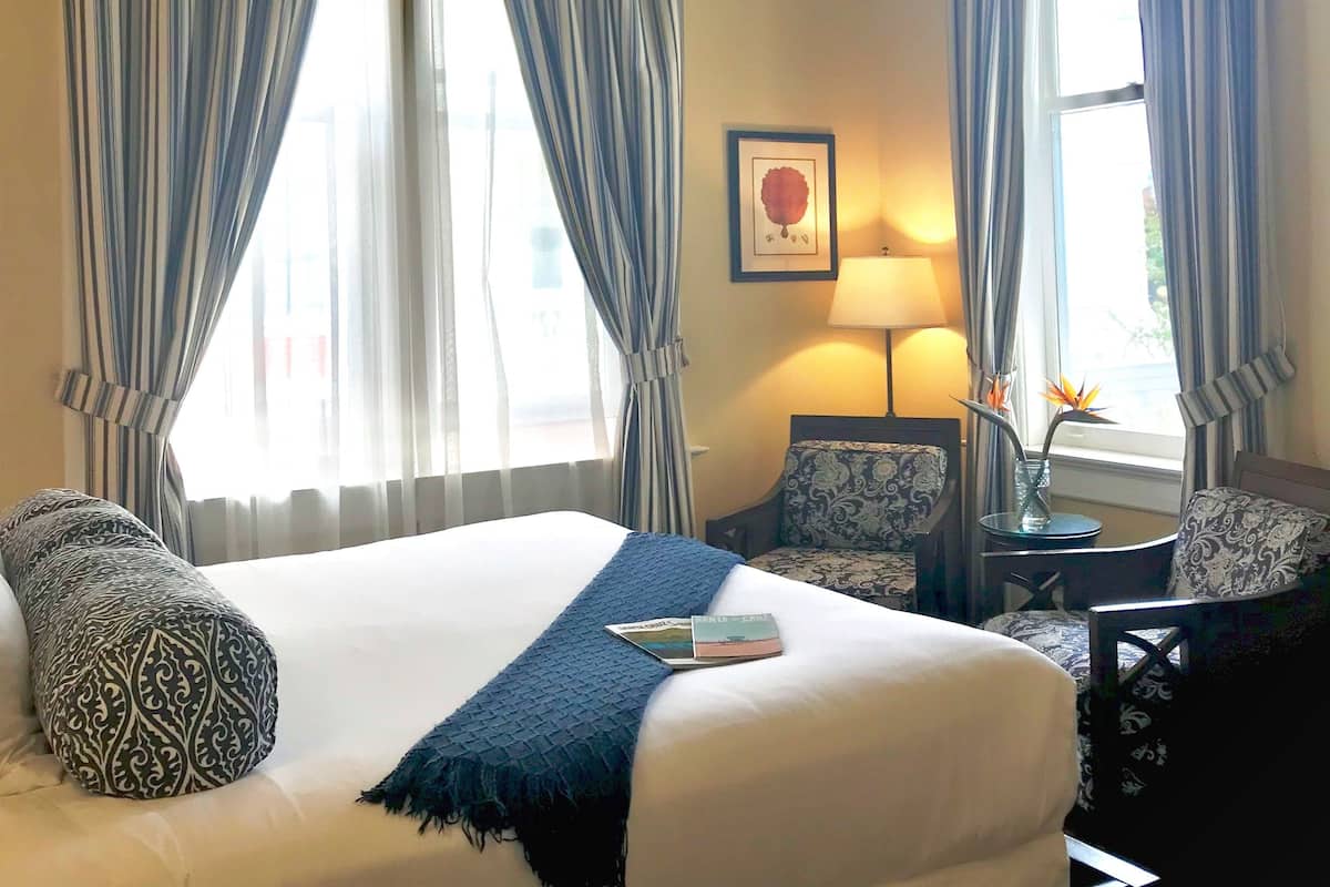 A hotel room with a large bed, two chairs, a table with a lamp, and a window with curtains.