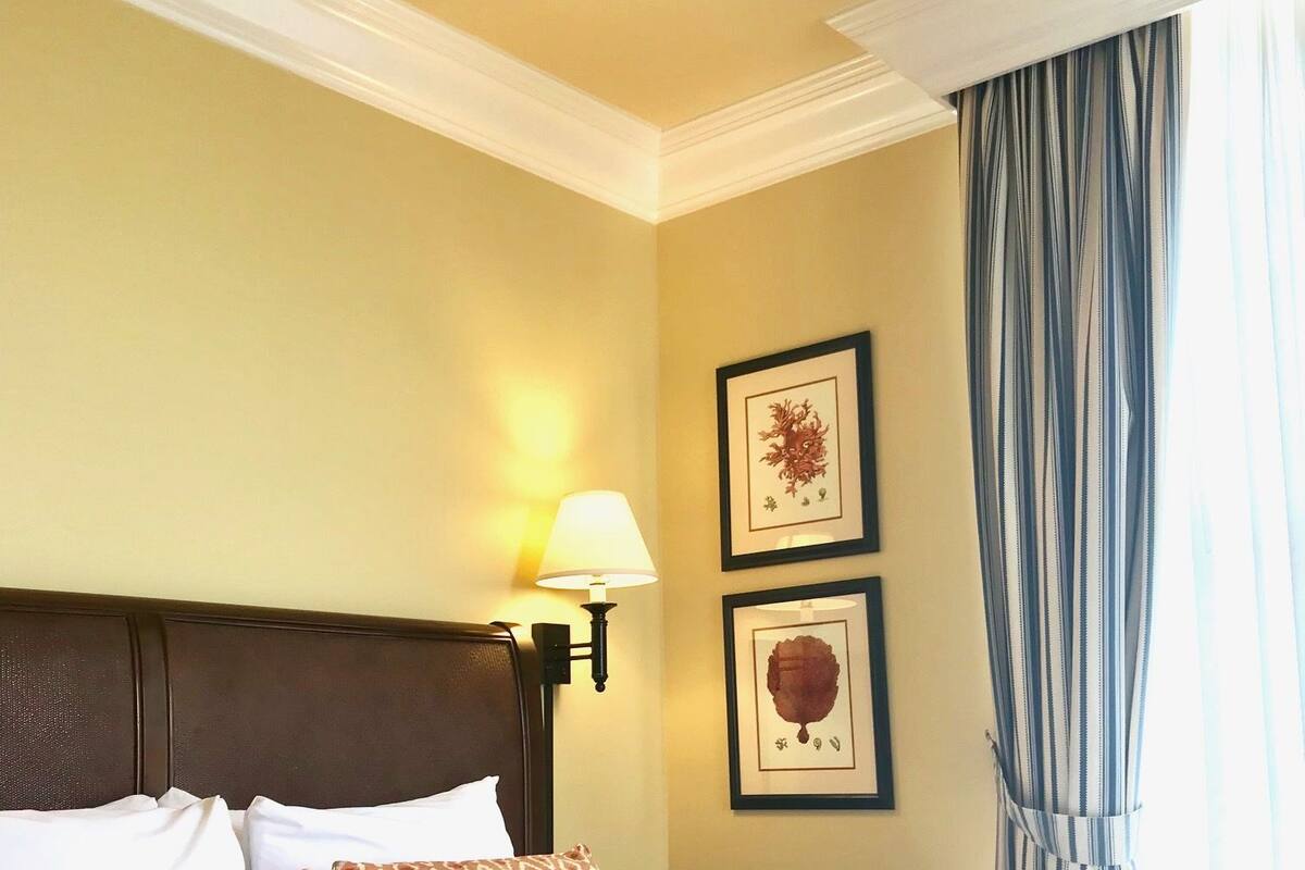A hotel room with a large bed, a headboard, two wall-mounted lamps, and two framed pictures.