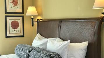 Ein Hotelzimmer mit einem Bett, zwei gerahmten Pflanzenbildern, einer Wandlampe und einem strukturierten Kopfteil.