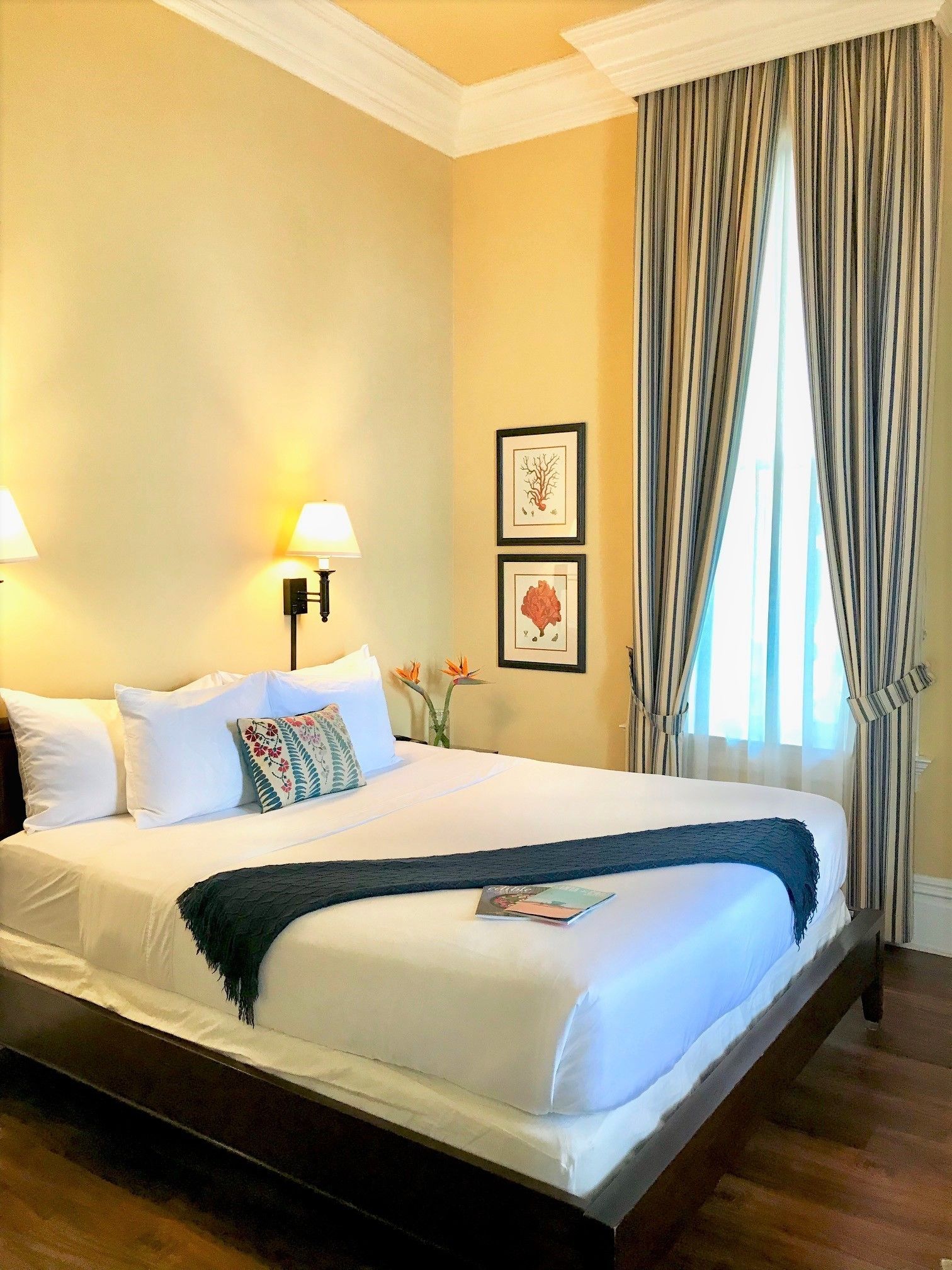 Habitación de hotel con una cama grande, dos lámparas de pared, una obra de arte enmarco y una ventana con cortinas.