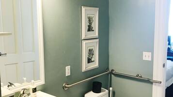 A bathroom with a white sink, a toilet, a handrail, and two framed pictures on the wall.