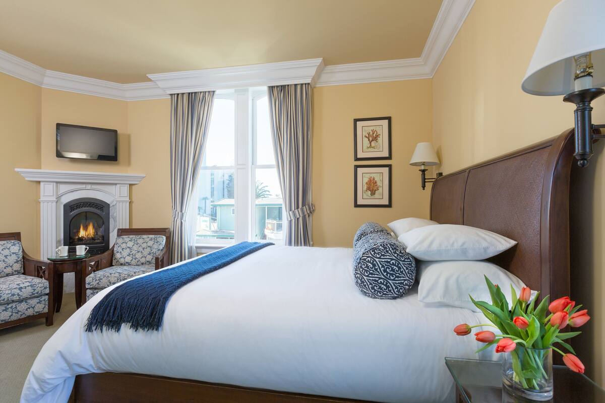 A hotel room with a large bed, a fireplace, a TV, and a view of the city.