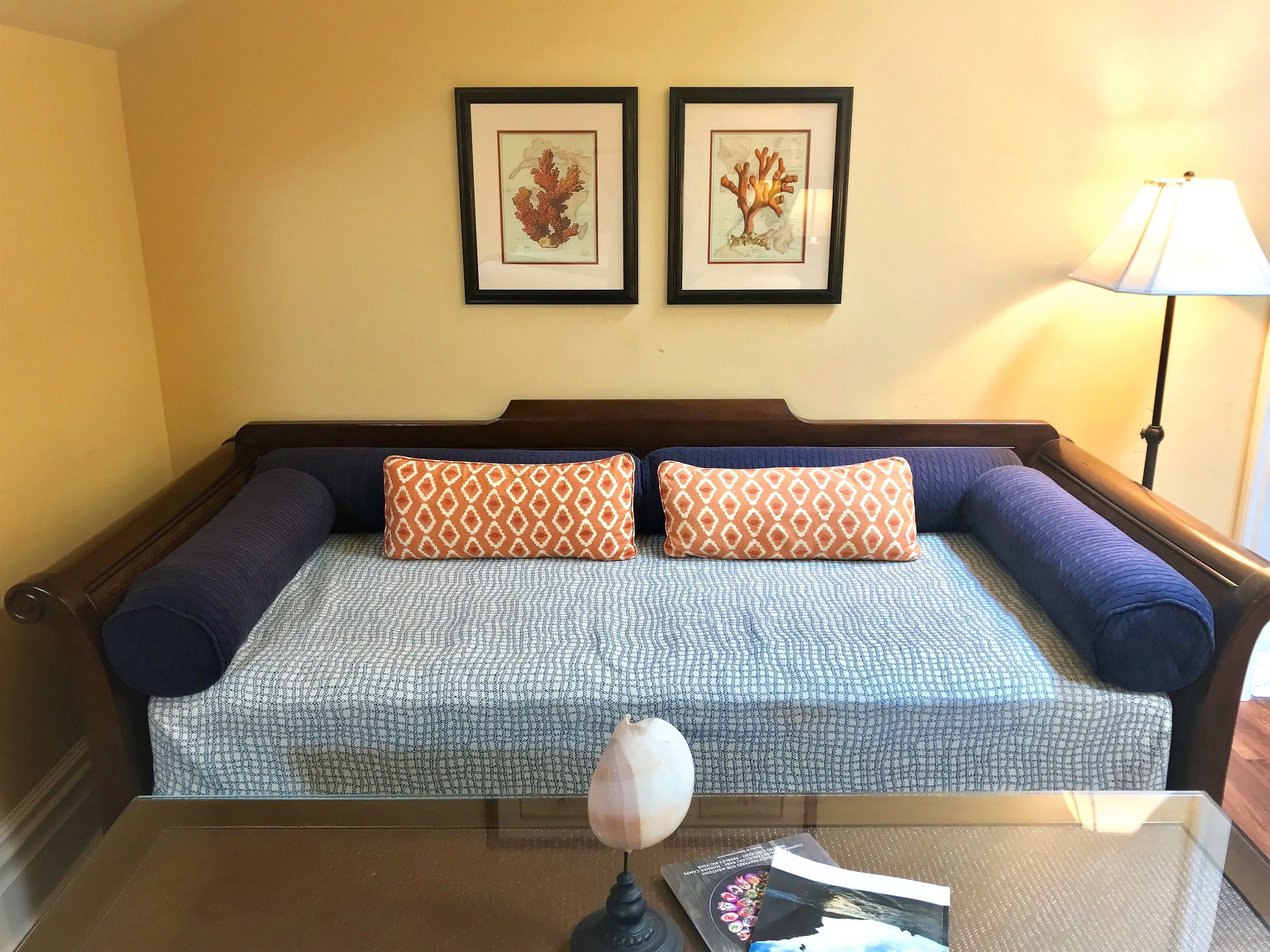 A bed with a patterned bedspread, two matching pillows, and a bedside table with a lamp and magazines.