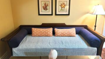 A bed with a patterned bedspread, two matching pillows, and a bedside table with a lamp and magazines.