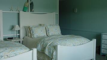 A bedroom with a white bed, a nightstand with a lamp, and a dresser.