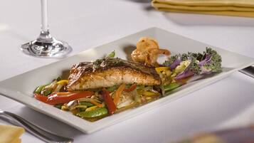 A dining table with a plate of fish, vegetables, and a glass of white wine.