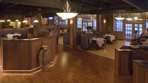 A restaurant with wooden flooring, a central bar area, and tables with white tablecloths. - Lake Opechee Inn and Spa (Laconia)