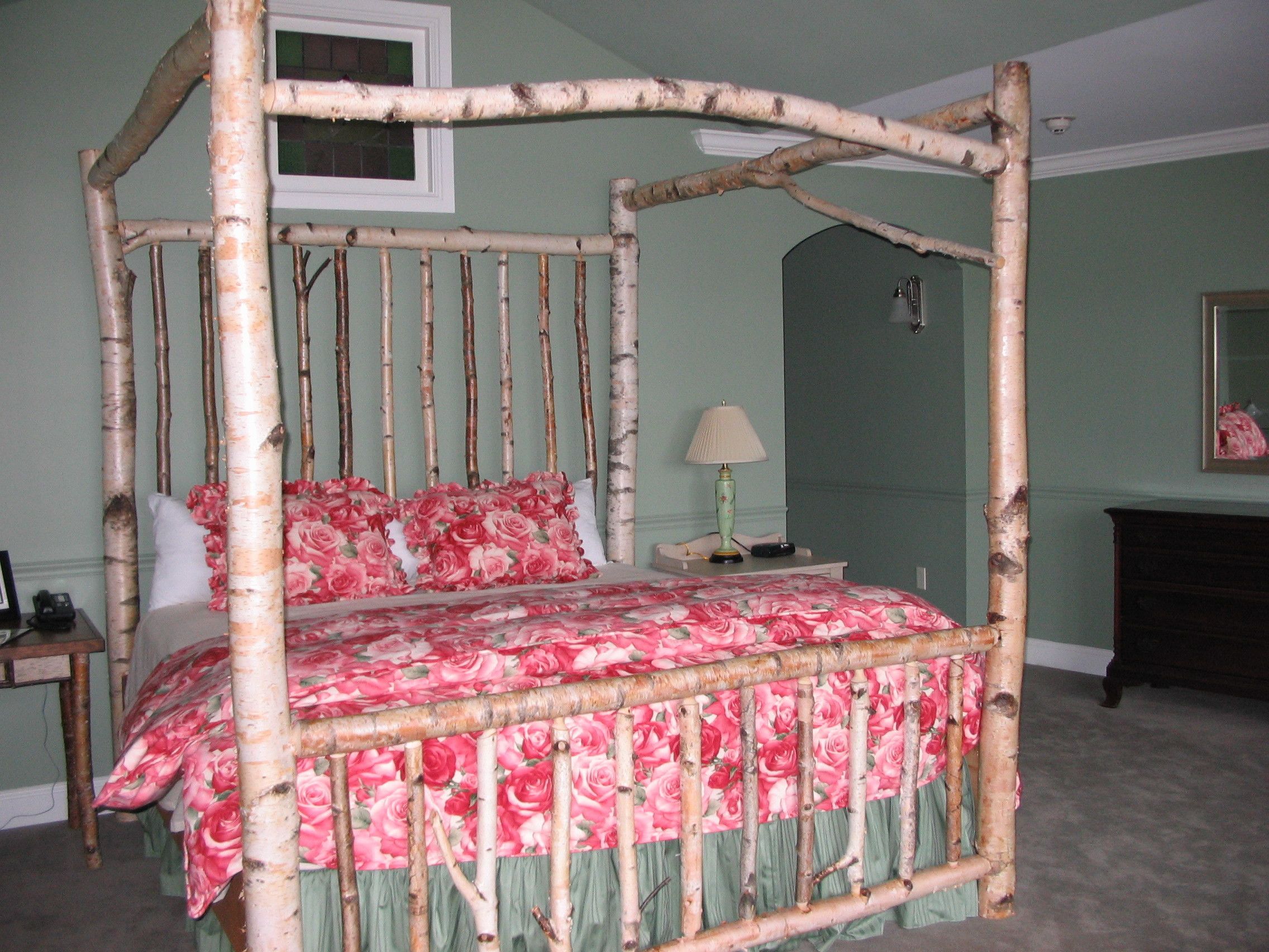A four-poster bed with floral bedding in a room with green walls and a mirror on the wall.