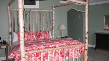 A four-poster bed with floral bedding in a room with green walls and a mirror on the wall.