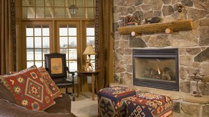 A cozy living room with a stone fireplace, leather sofa, patterned ottomans, and a view through large windows. - Lake Opechee Inn and Spa (Laconia)