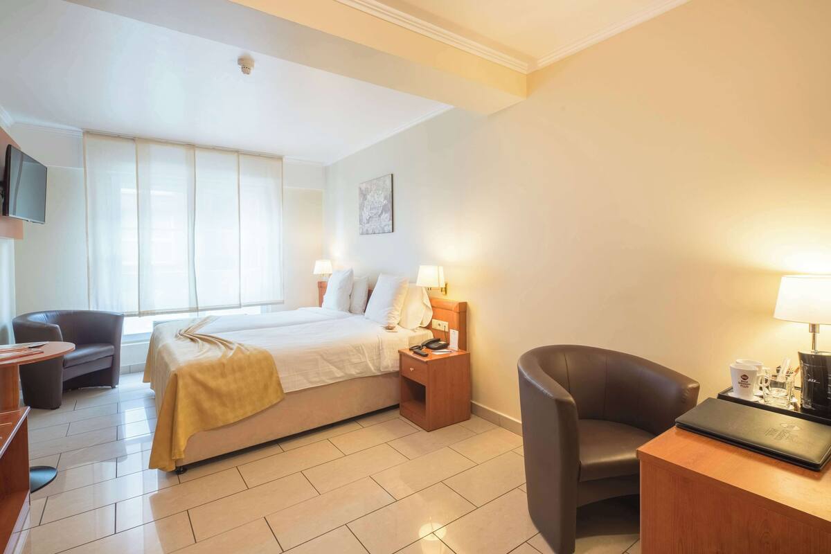 A hotel room with a bed, bedside tables, a desk, a chair, and a television.