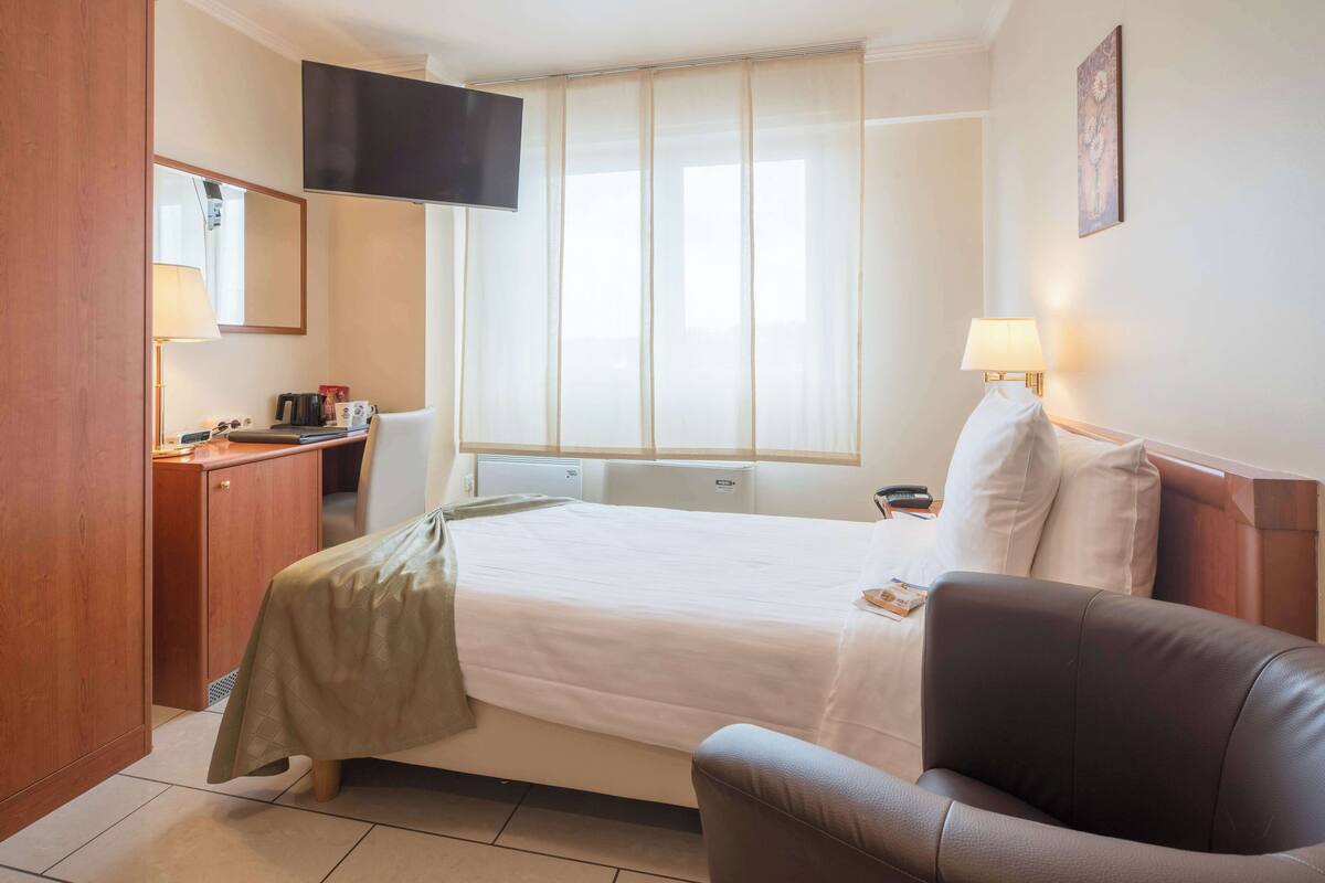A hotel room with a bed, a desk, a chair, a TV, and a window with curtains.