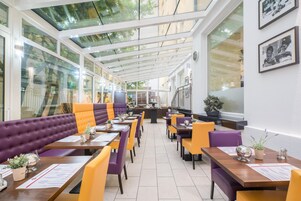 Un restaurante con techos altos, paneles de vidrio y una combinación de asientos morados y amarillos.