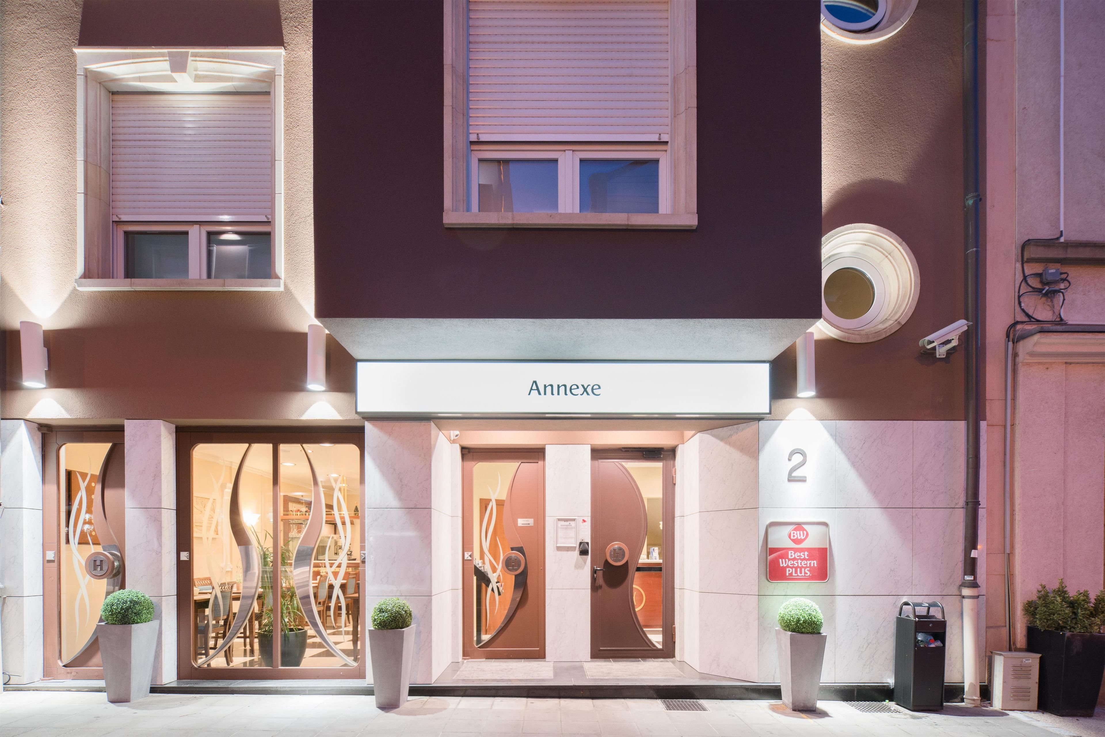 A hotel entrance with a modern design, including a large glass door, a sign reading 'Anex', and a number '2' indicating the building's location.
