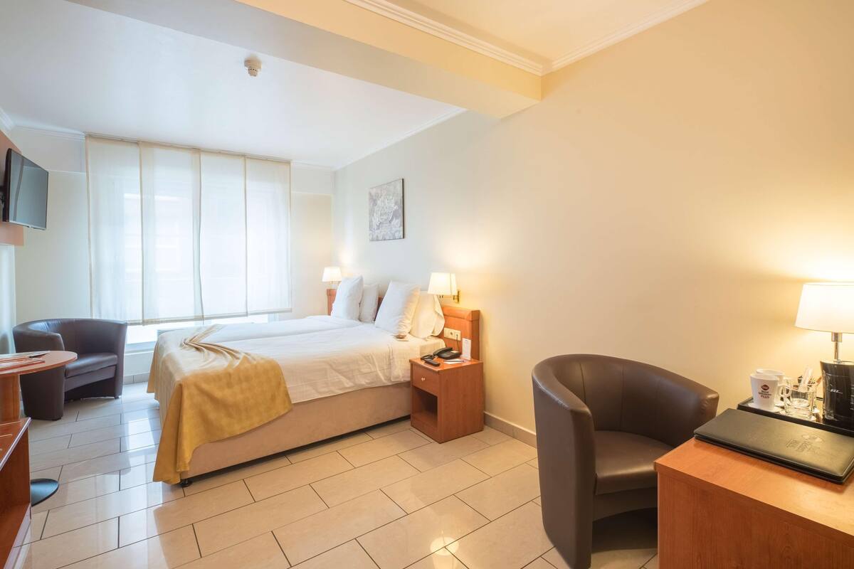 A hotel room with a bed, bedside tables, a desk, a chair, and a TV.