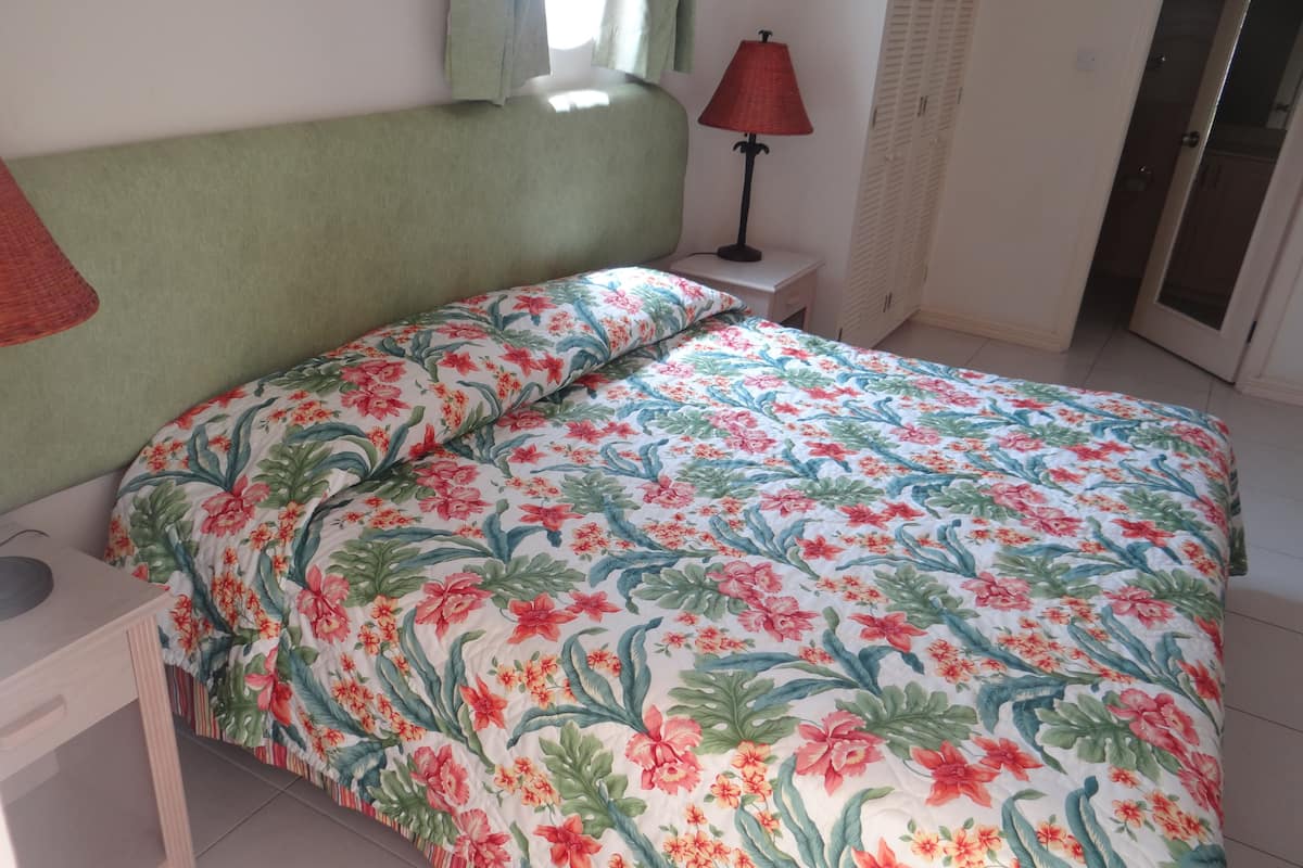 Un dormitorio con edredón estampado con flores, una mesita de noche, una lámpara y un armario.