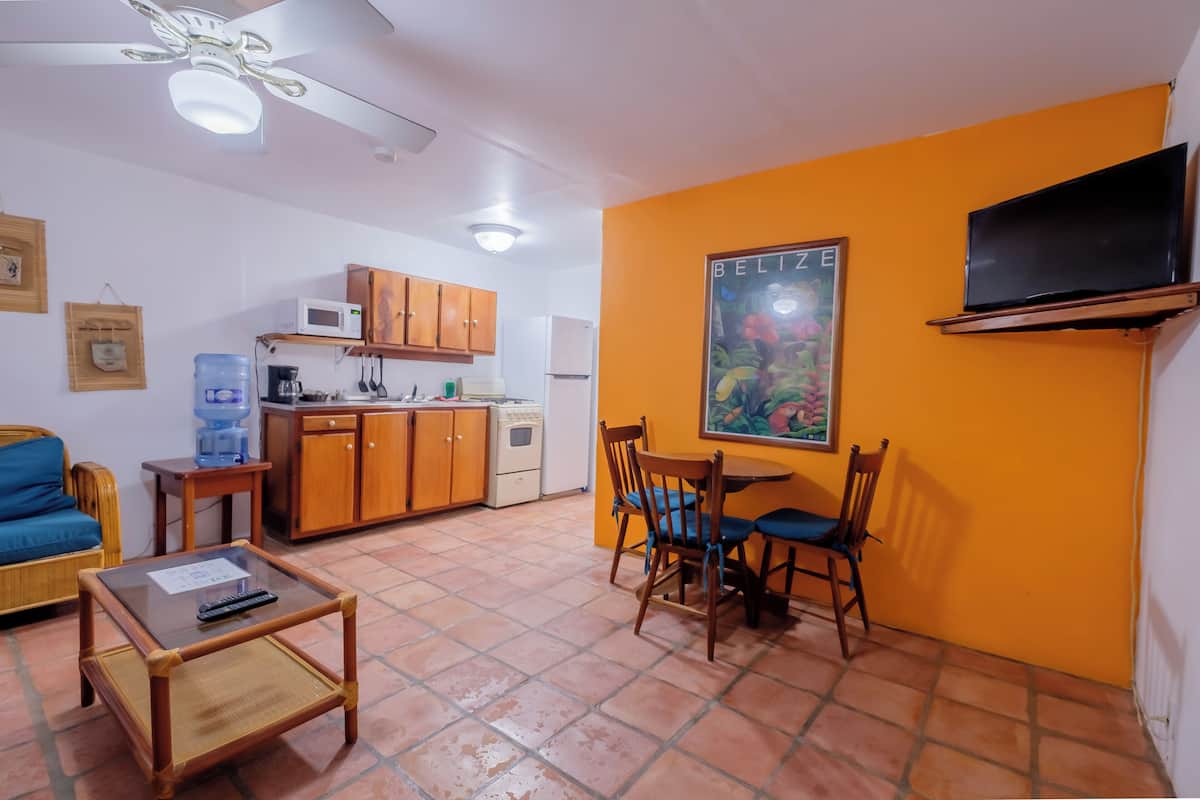 Un espacio habitable compacto con kitchenette, una zona de comedor con sillas, un televisor montado en la pared y un ventilador de techo.