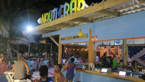 An outdoor bar area with a wooden structure labeled "Nauticrab" and a sign reading "Belikin My Beer." - Seven Seas Resort (San Pedro)
