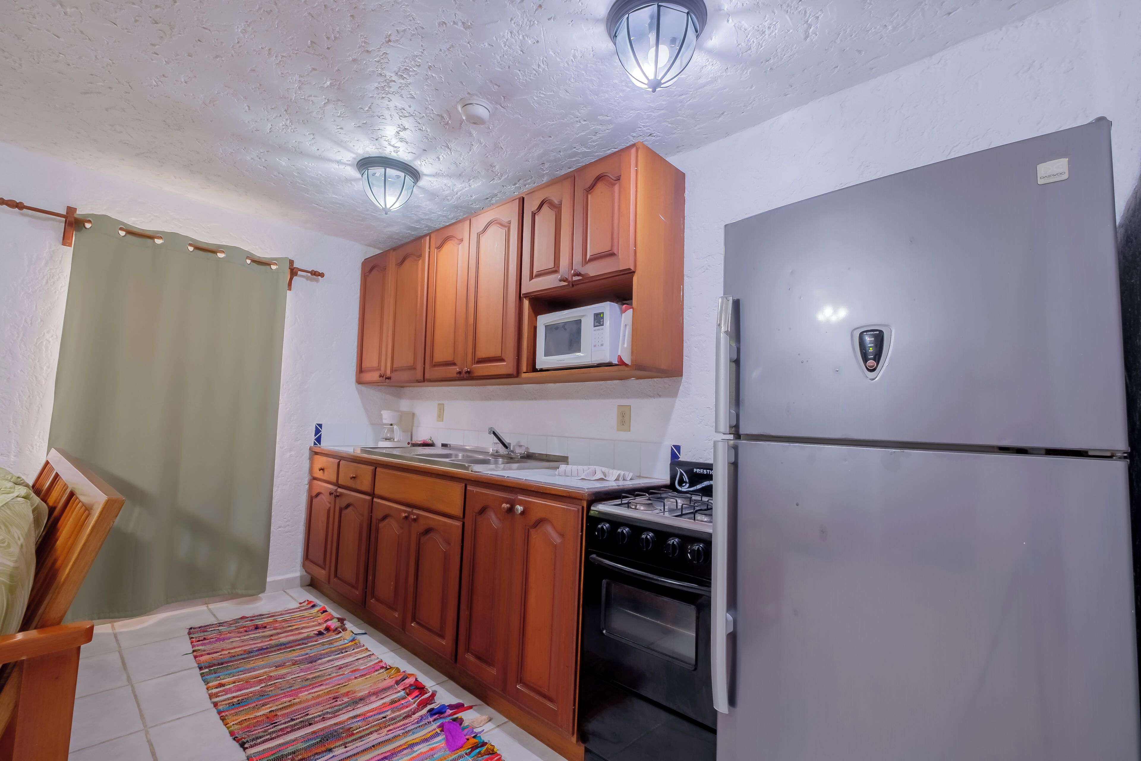 A compact kitchen with wooden cabinets, a stainless steel refrigerator, a microwave, and a gas stove.