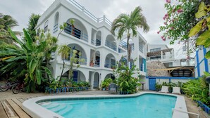 A pool area with a white building featuring arched balconies and blue railings, surrounded by tropical plants and a bicycle. - Seven Seas Resort (San Pedro)