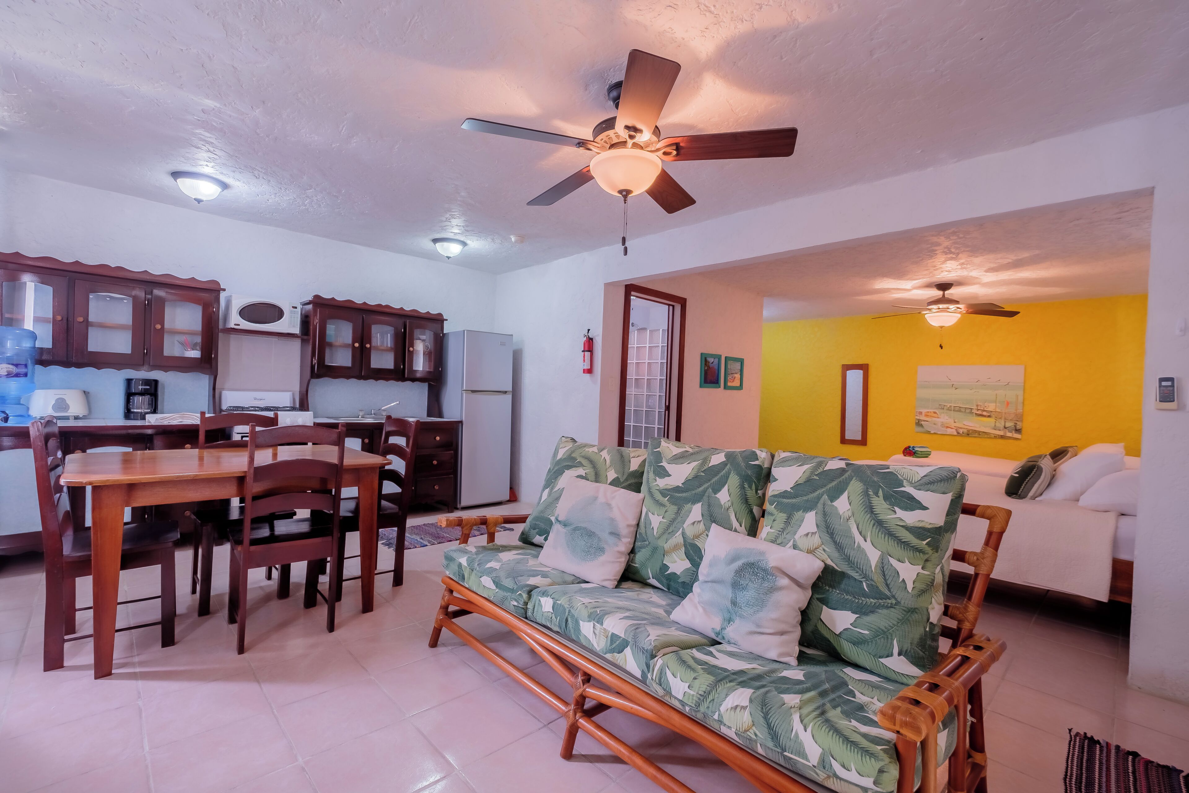 A living room with a sofa, dining table, chairs, and a kitchen area with cabinets and appliances.