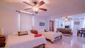 A hotel room with two beds, a ceiling fan, a TV, and a dining area. - Seven Seas Resort (San Pedro)