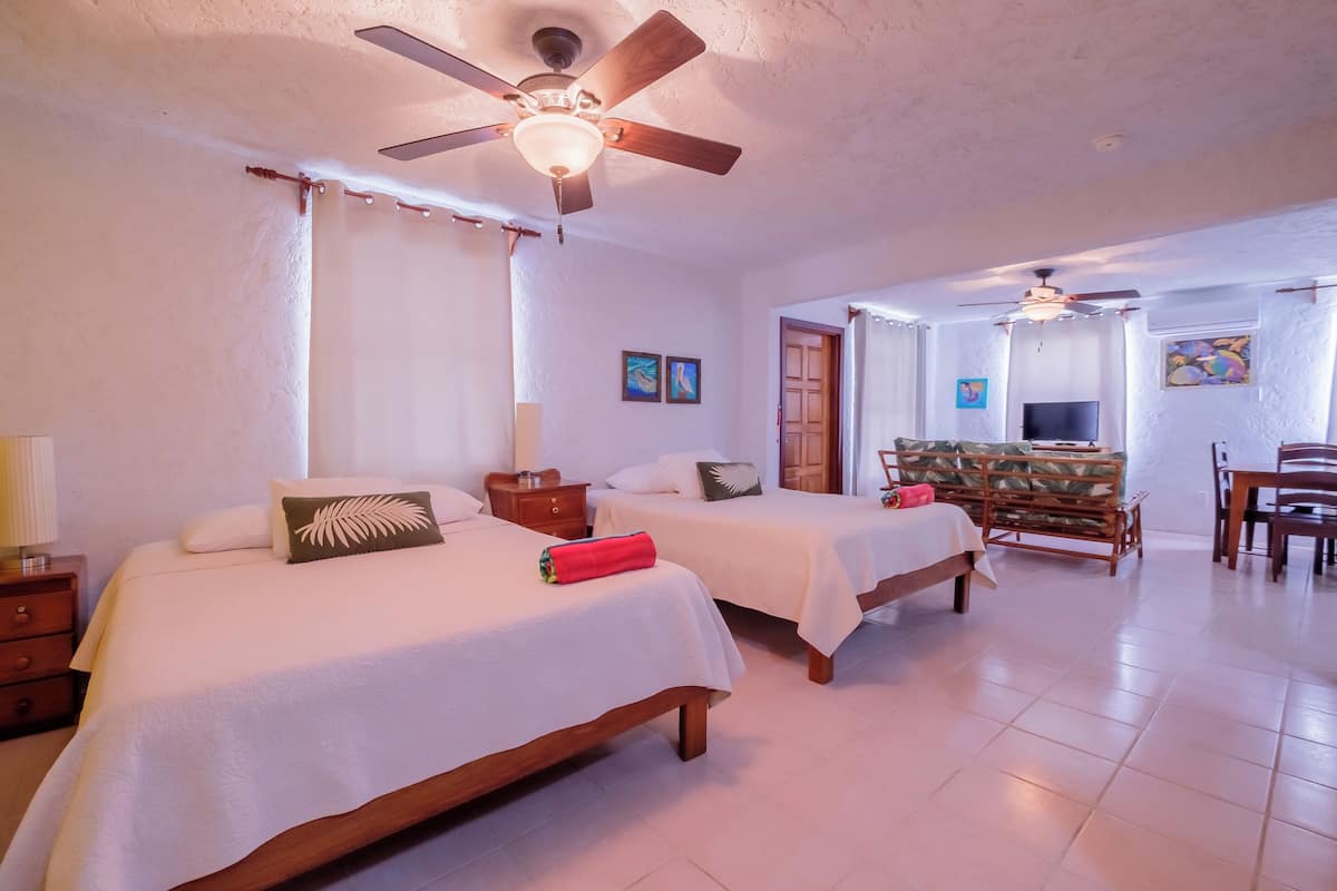 Habitación de hotel con dos camas, ventilador de techo, televisor y zona de comedor.