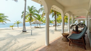 Zona de playa techada con palmeras, una silla de descanso y vista al océano.