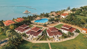 Un resort con varias edificaciones blancas, una piscina central y vista al océano.