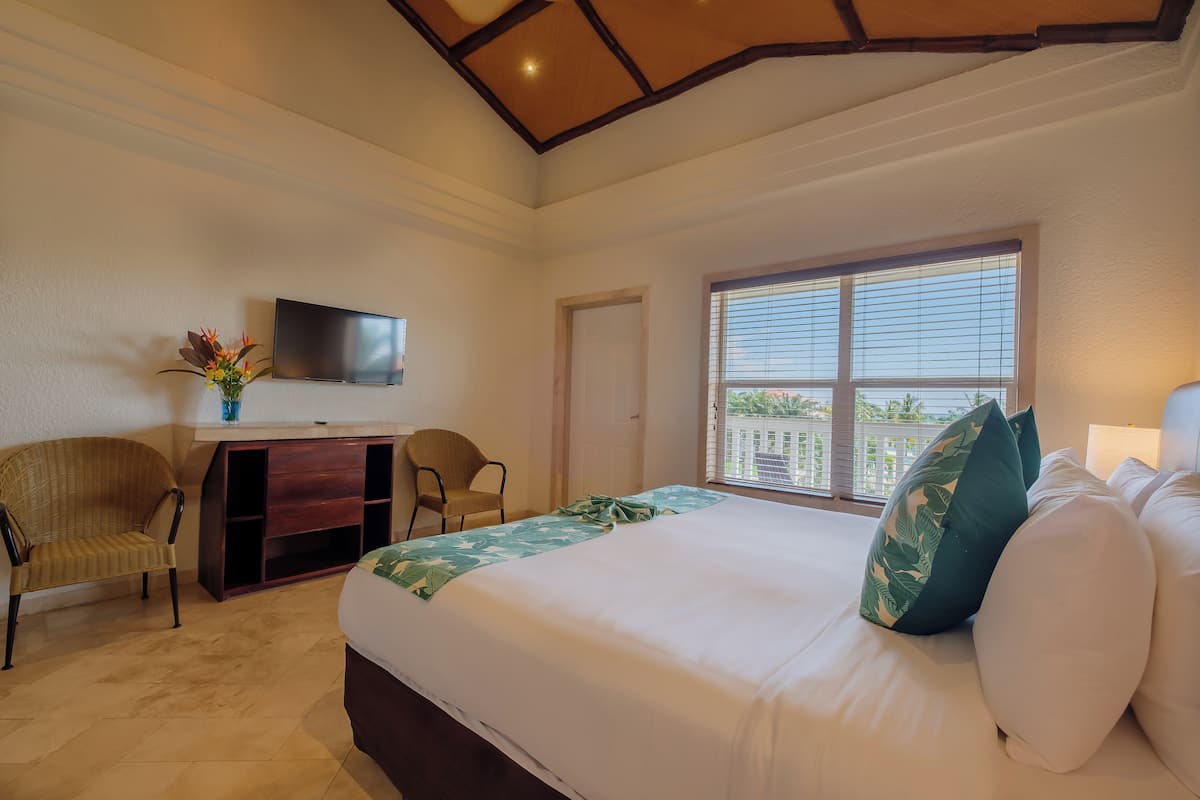 A hotel room with a bed, a desk with a chair, a TV on the wall, and a window with blinds.