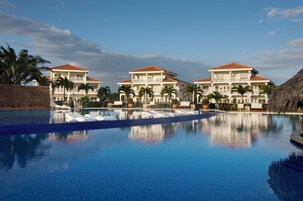 Un resort con una piscina grande, varias edificaciones con techos de tejas rojas y palmeras.
