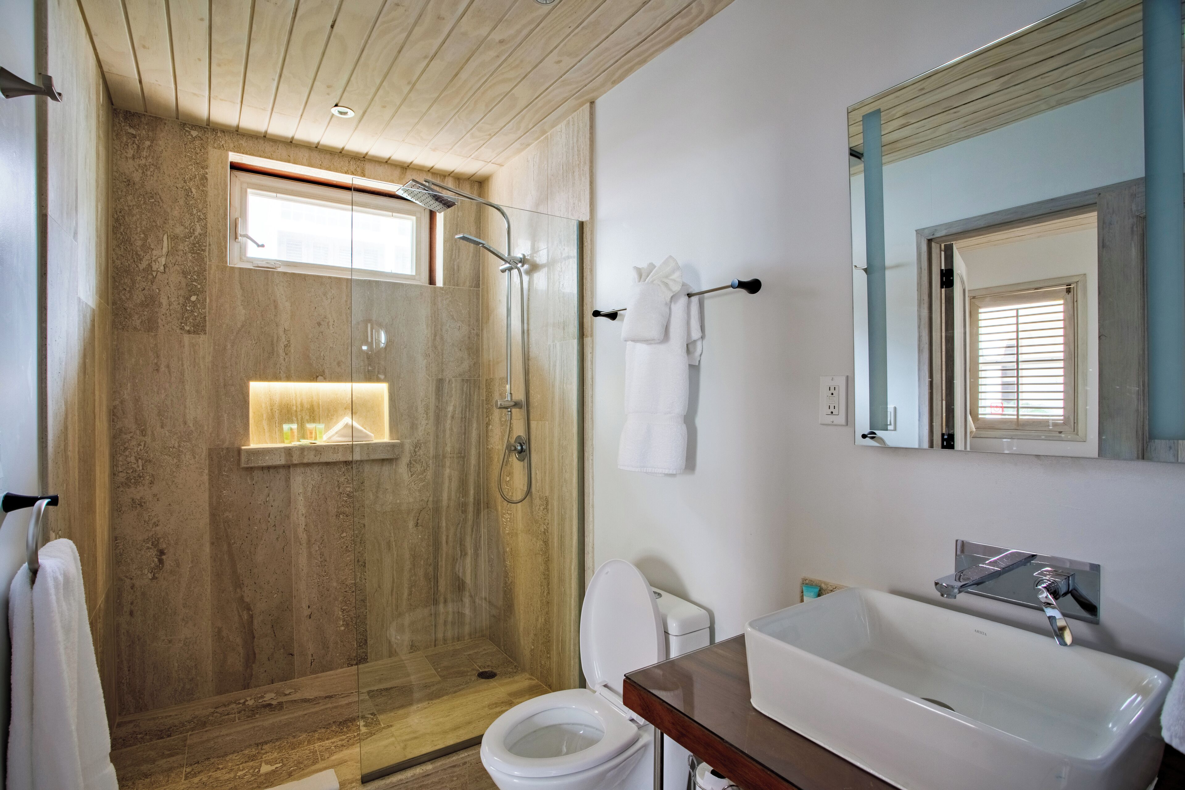 A modern bathroom with a glass-enclosed shower, a white toilet, and a large sink with a mirror above it.