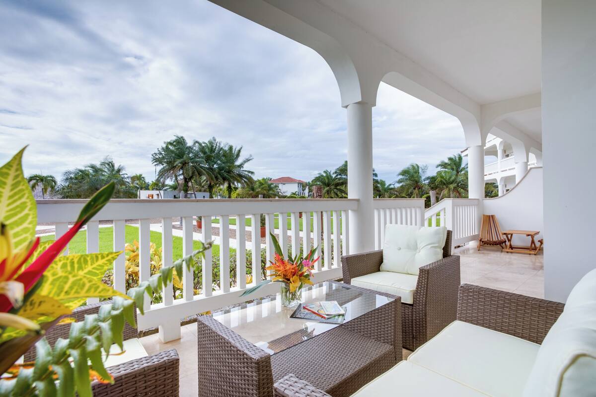 A covered outdoor seating area with wicker furniture, a glass table, and a white railing.