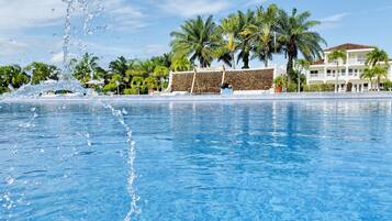 Een helderblauw zwembad met opspattend water, omringd door palmbomen en een gebouw met de tekst 'The Placencia'.