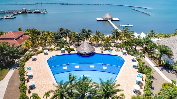 Un resort con piscina central, palmeras y vistas al océano.