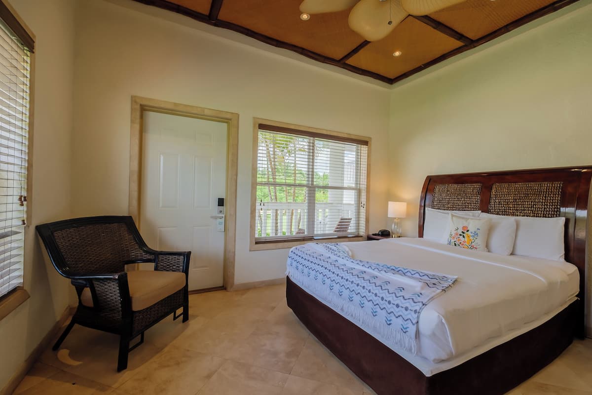 A bedroom with a bed, a chair, a door, and a window with blinds.