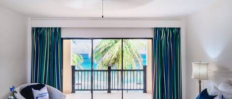 A hotel room with a bed, a chair, a table, and a view of the ocean through a balcony.