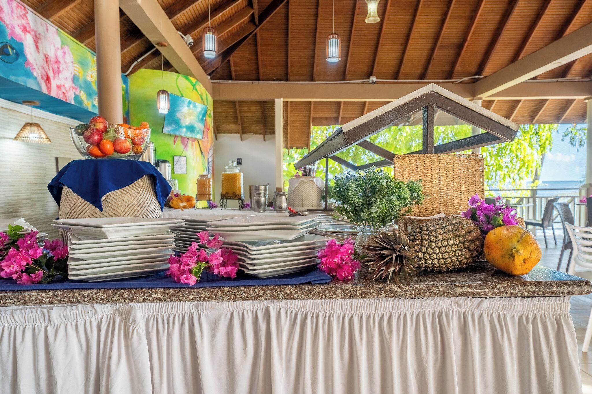 Un espace extérieur abrité, aménagé pour les repas, avec une table dressée, et entouré de plantes et de fleurs tropicales.