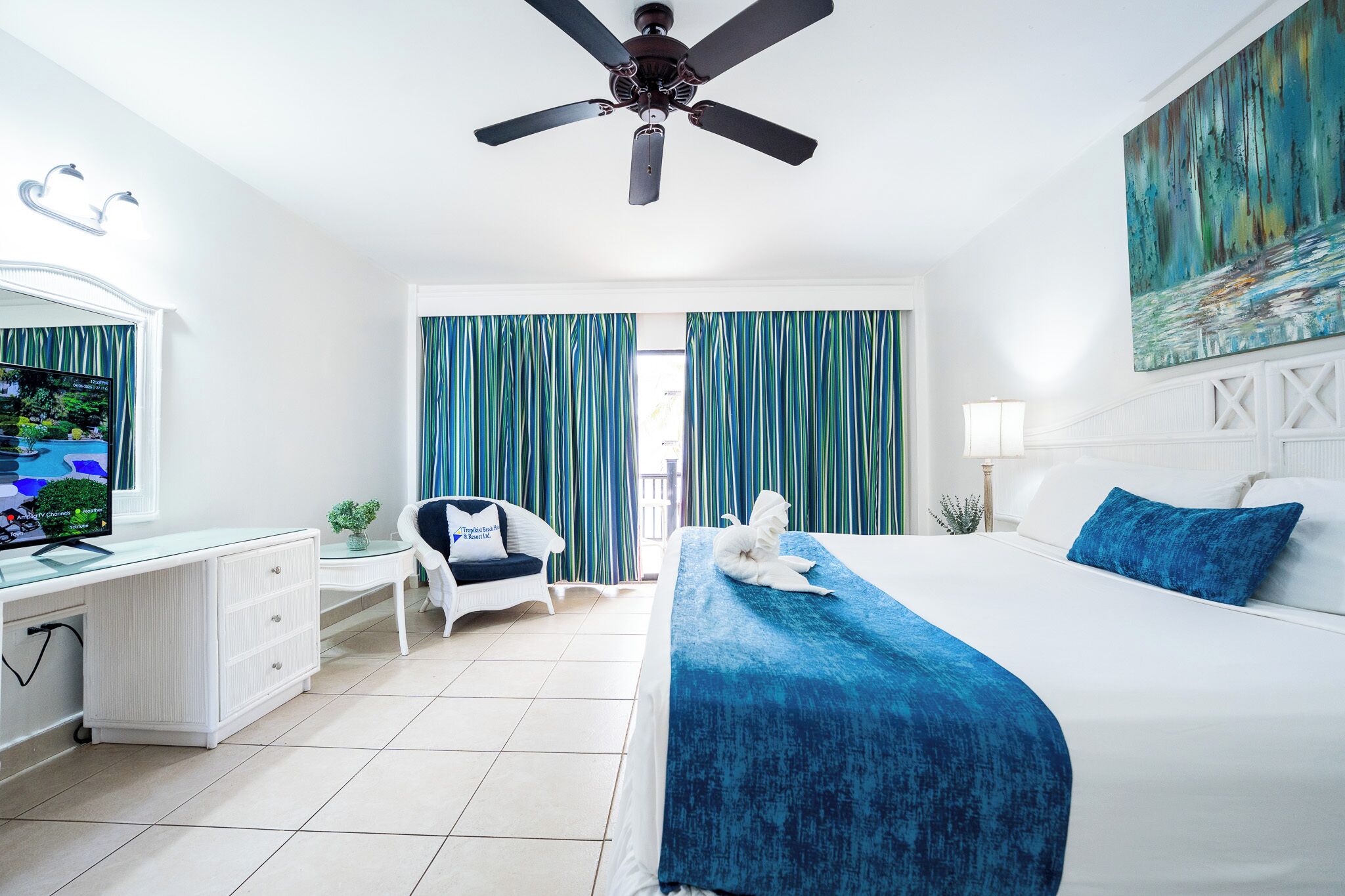 Ein Hotelzimmer mit Bett, Schreibtisch, Stuhl, Deckenventilator und Vorhängen.