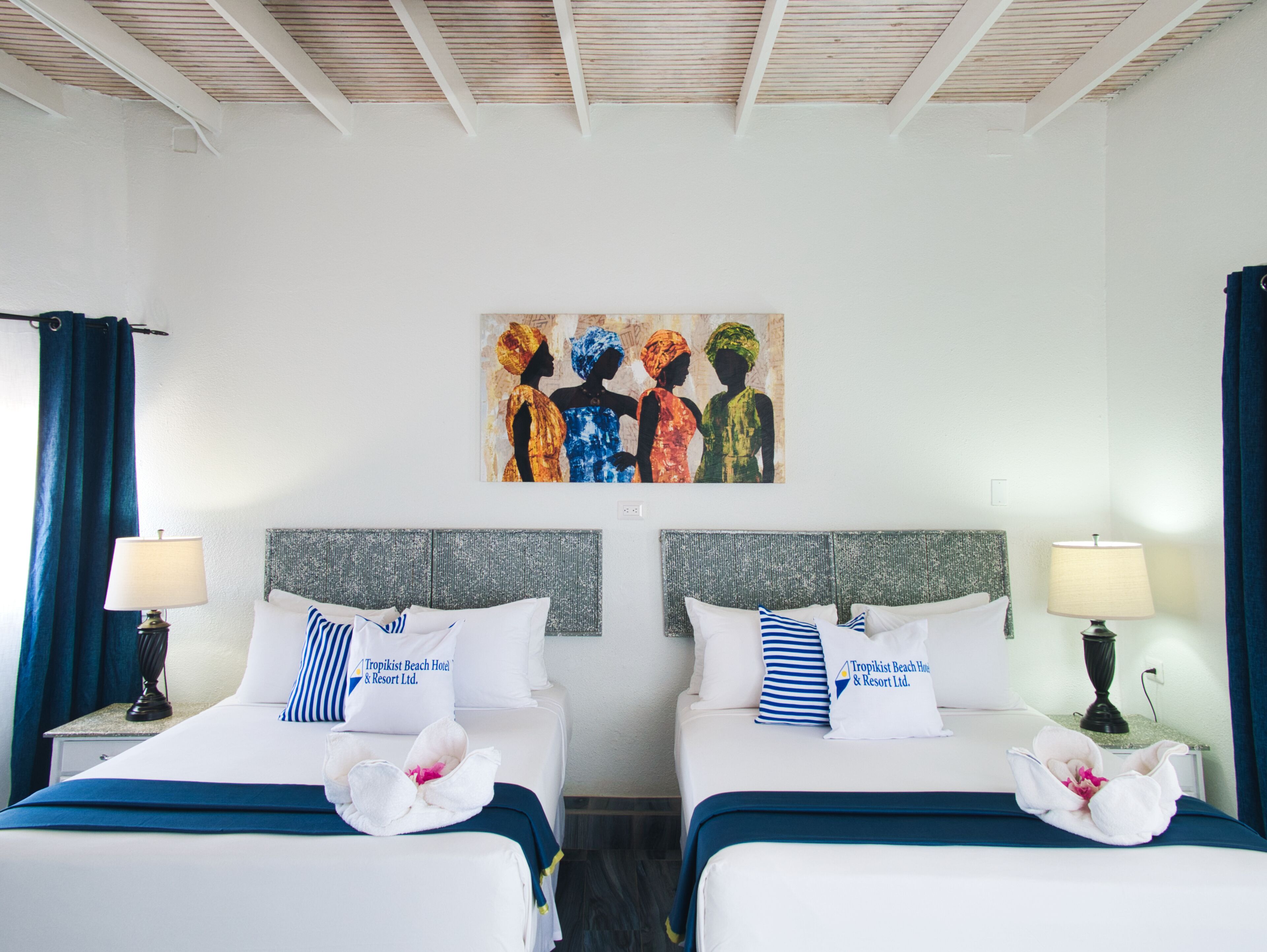 Quarto de hotel com duas camas, cada uma com cabeceira, almofadas e uma toalha sobre a cama. Há um quadro na parede acima das camas.