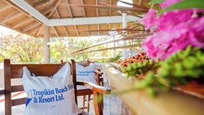 A wooden bench with a white pillow labeled "Tropikist Beach & Resort Ltd." and a potted plant with pink flowers. - Tropikist Beach Hotel & Resort (Crown Point)