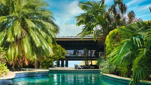 A swimming pool with clear blue water, surrounded by lush palm trees and tropical plants. - Tropikist Beach Hotel & Resort (Crown Point)