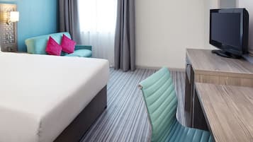 Une chambre d’hôtel avec un lit, un bureau avec une télévision, une chaise et une fenêtre avec des rideaux.