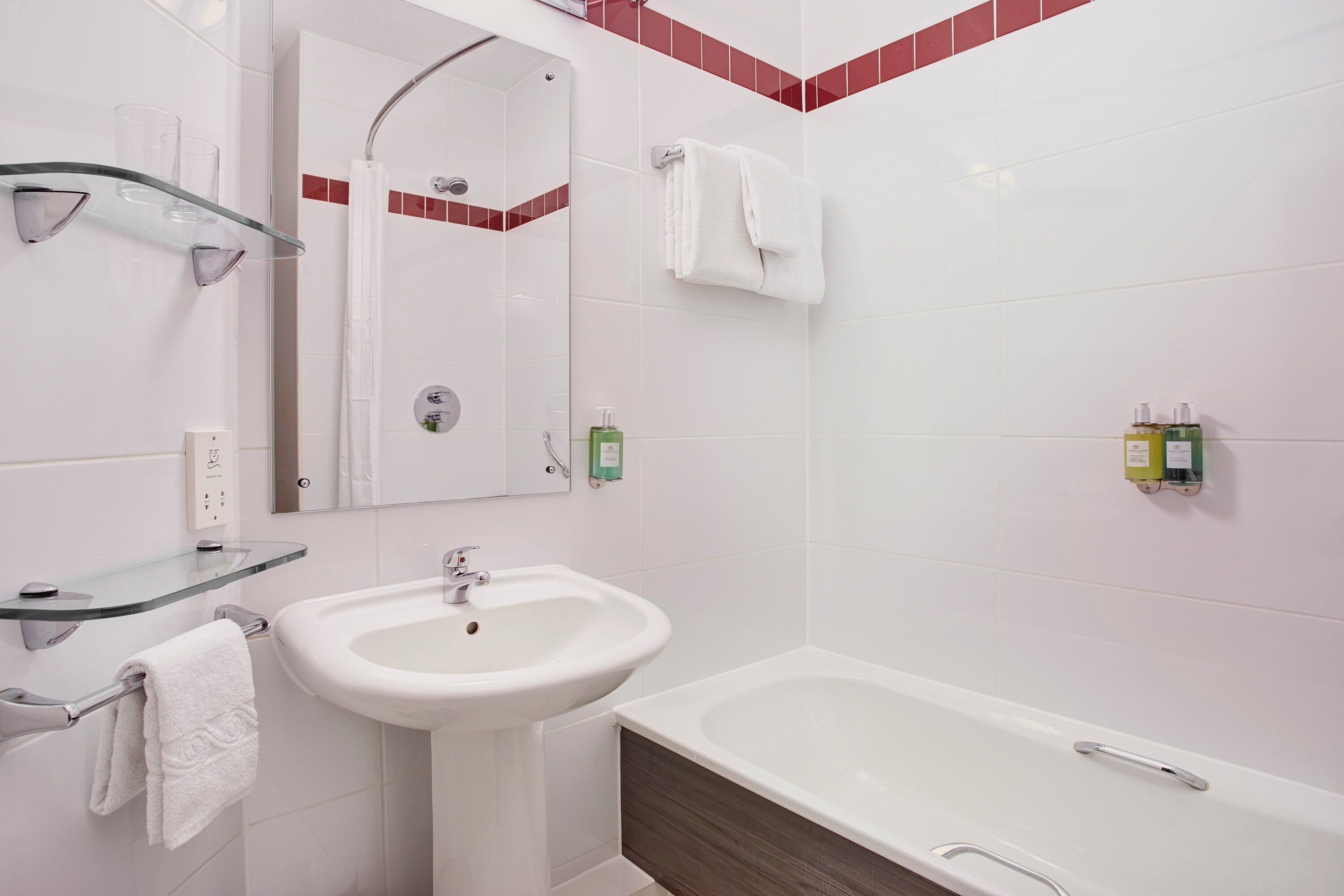 Ein modernes Badezimmer mit einem weißen Waschbecken, Glastablaren, einem Spiegel, einer Badewanne und roten Fliesenakzenten.
