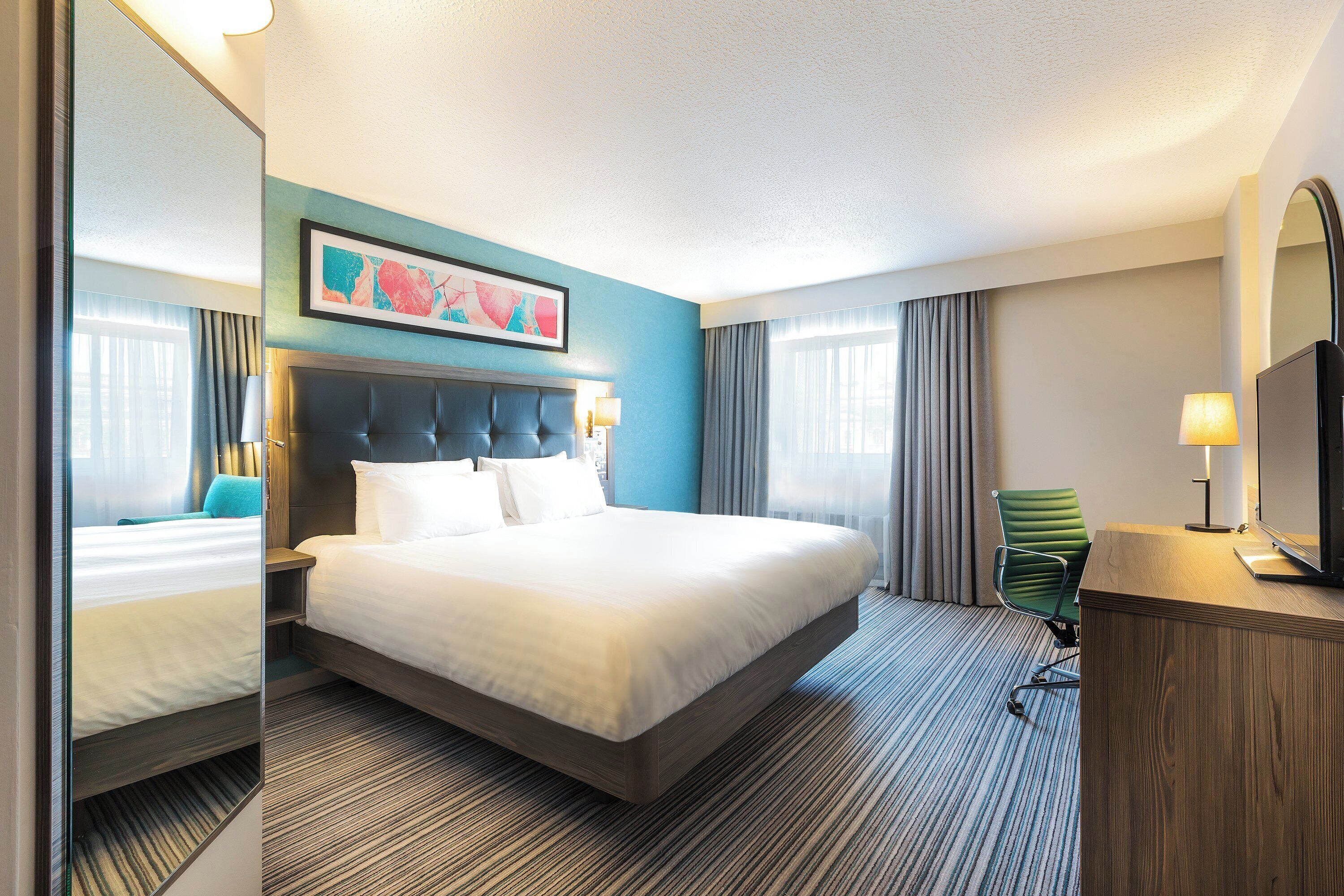 A hotel room with a large bed, a desk, a chair, and a television.