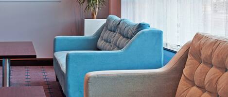 Una sala moderna con un sofá azul, un sillón marrón, una mesa de centro de madera y una planta en maceta.