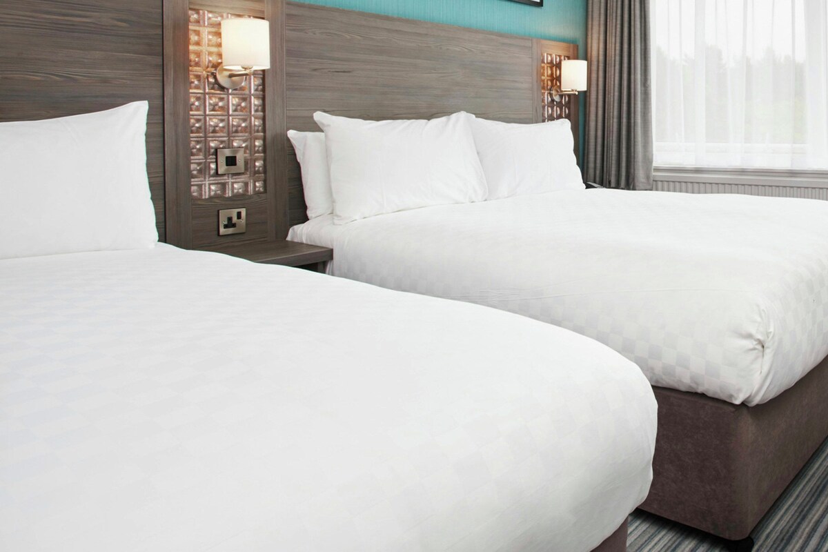 A hotel room with two beds, a wooden headboard, and a window with curtains.