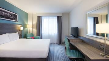 Una camera d'albergo con un letto grande, una scrivania con televisore, una sedia e una finestra con tende.