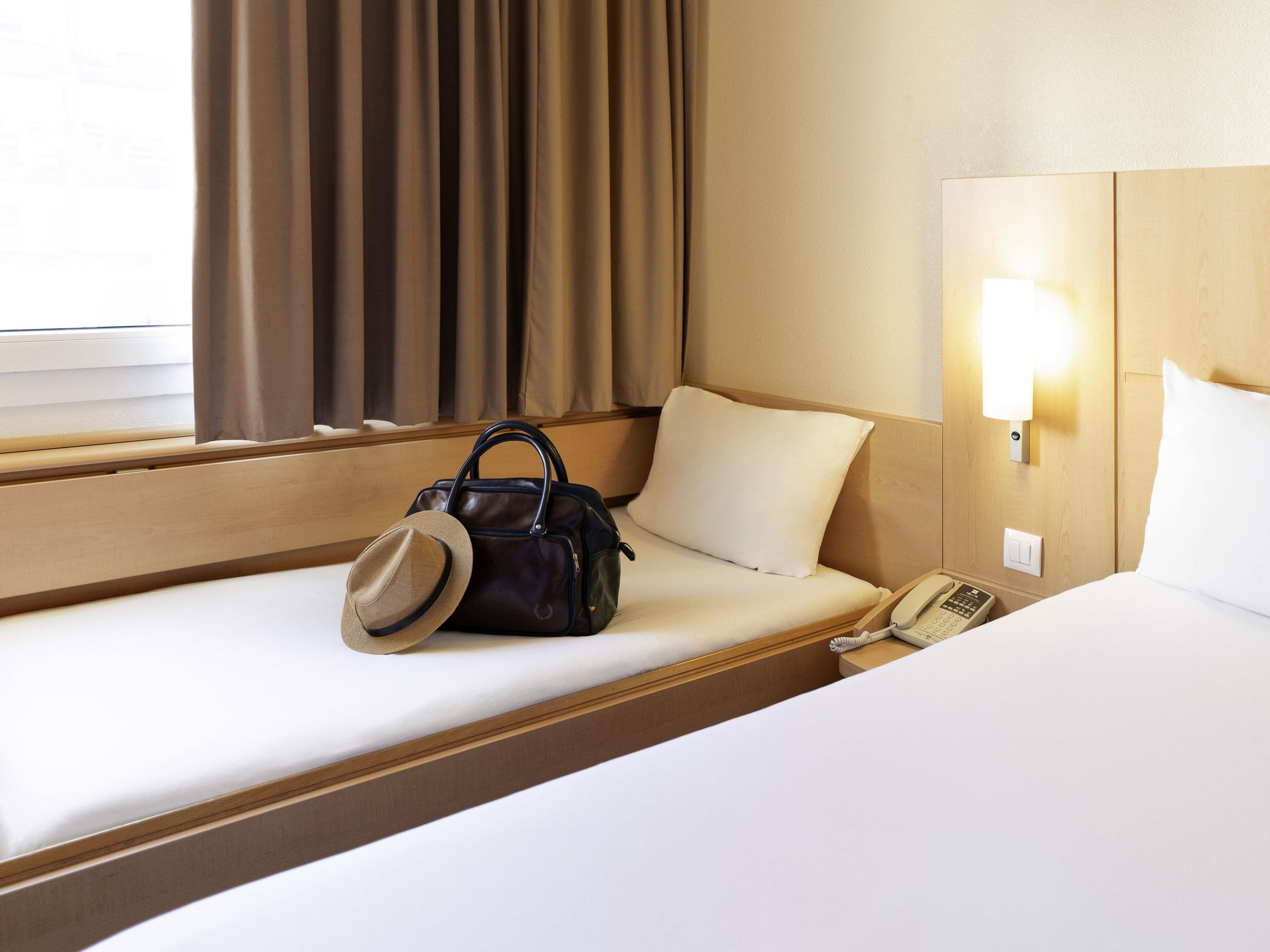 Hotelkamer met een enkel bed, nachtkastje met lamp, telefoon en handtas op het bed.