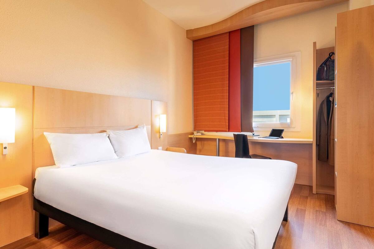 Een hotelkamer met een groot bed, bedlampen, een bureau met een laptop en uitzicht op de lucht.